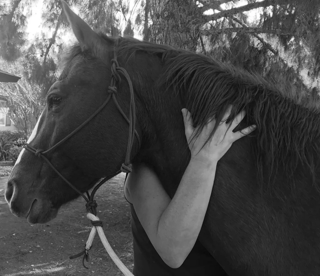 Grayscale image of human harm hugging the neck of a horse from the side view.